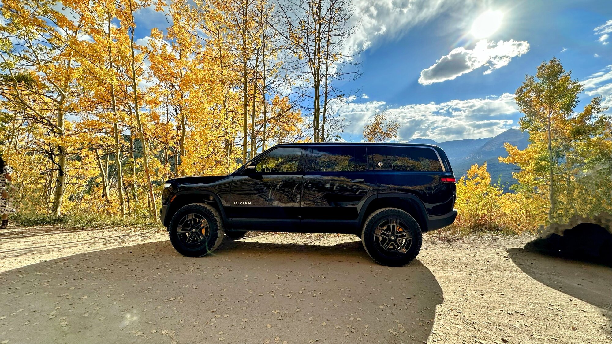 Rivian R1S parked among golden aspens with mountains behind
