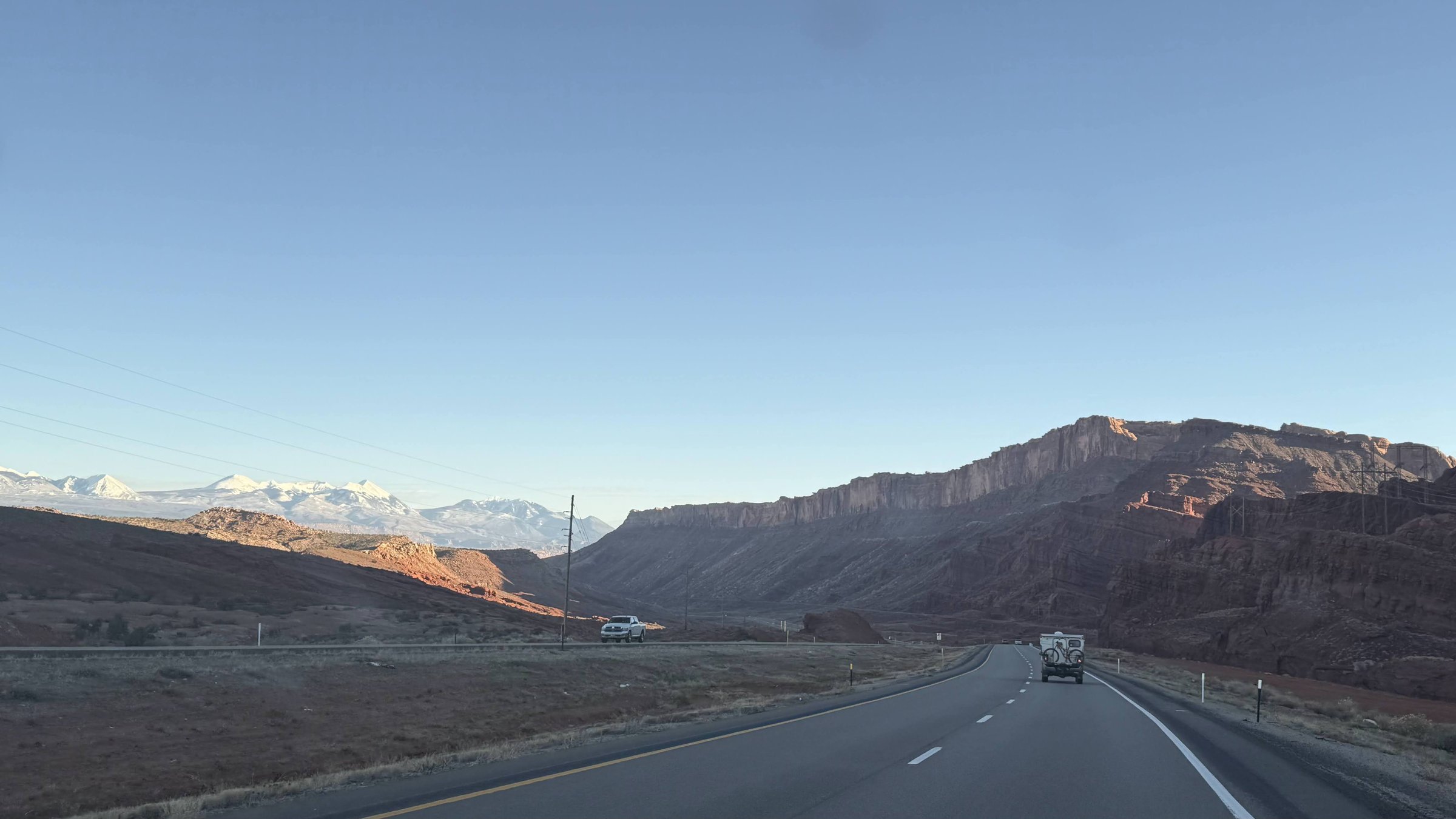 Road approaching Moab with red rock cliffs and snow-capped La Sal Mountains