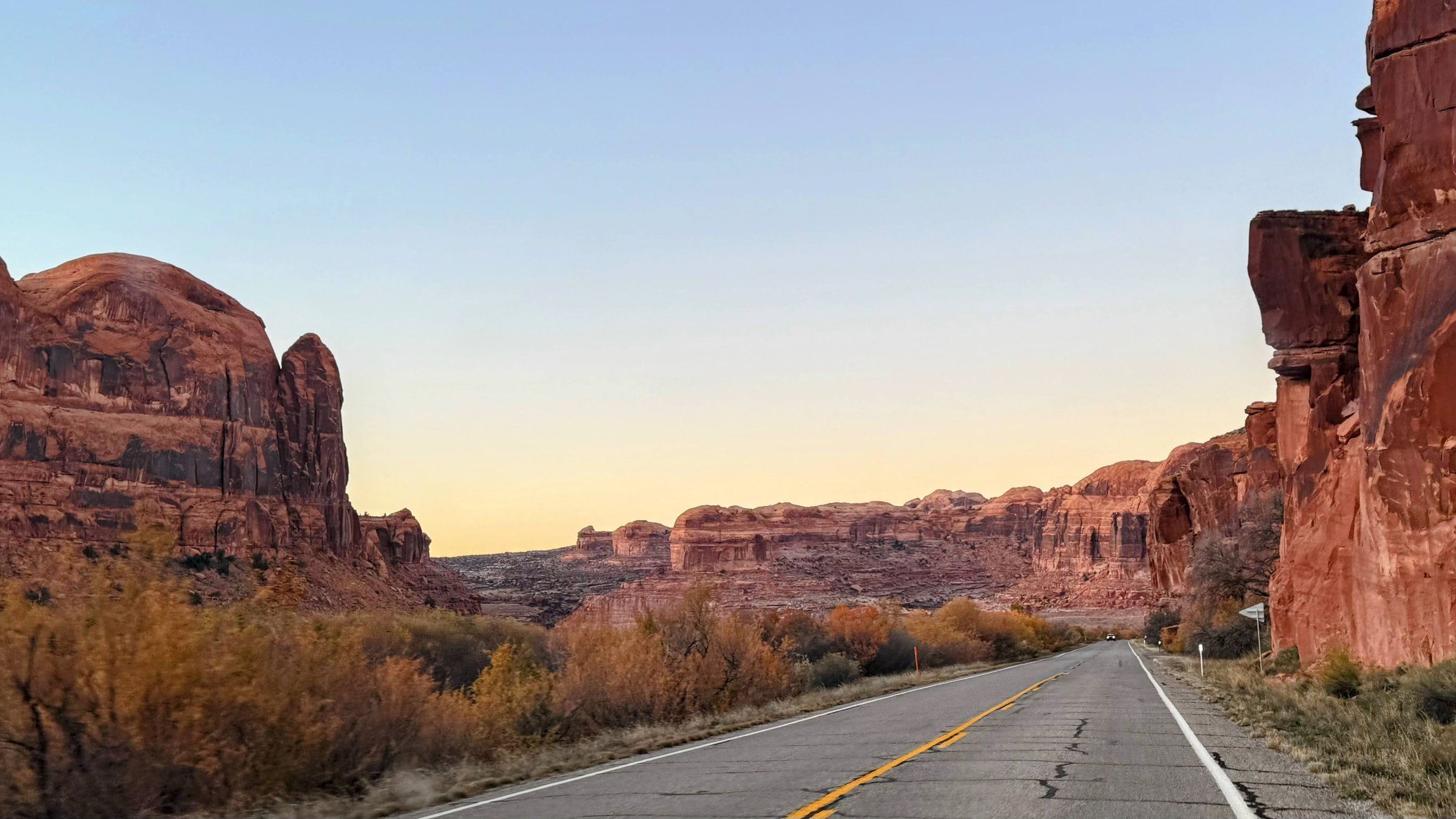 Road through Moab canyon at dusk with towering red rock walls on both sides